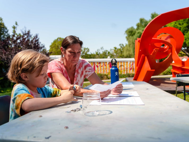A mother and child participate in an art activity next to a bright red sculpture