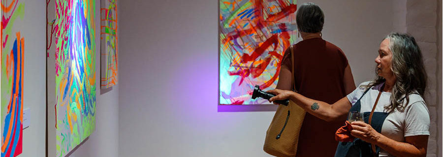 A woman in a gallery shines a UV flashlight at an artwork with phosphorescent paint