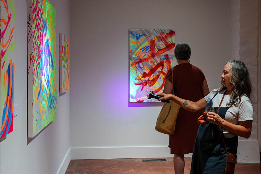 A woman in a gallery shines a UV flashlight at an artwork with phosphorescent paint