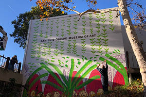 A man paints a brightly colored nature-inspired mural on the side of a building
