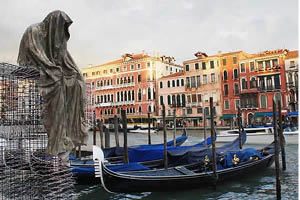 A large sculpture of a seated hooded figure overlooks the Venice canals and barges
