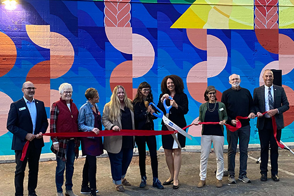 9 people cut a ceremonial ribbon for Maria Molteni's mural in downtown SLO, 