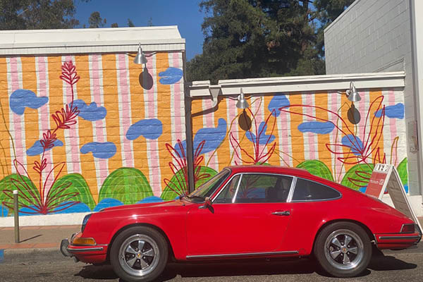 an old red Porsche is parked in front of the Museum of Art on Broad Street, a nice complement to the bright and colorful mural behind it