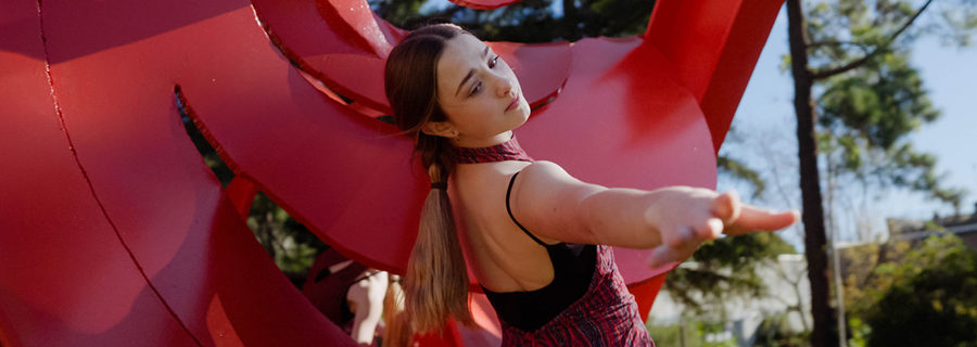 Performance of "Spira" by Maartje Herman of the Movement Arts Collective. Photo courtest Heraldo Creative Studios. A young woman in a red pantsuit and ponytail dances among the curves of a red steel sculpture by Mark di Suvero.