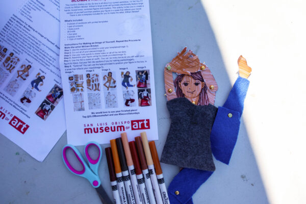 An example of the materials included in SLOMA's art kits: bilingual instructions, scissors, markers, and a finished example of a self-portrait figure