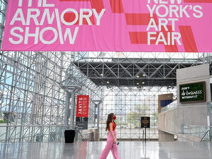 The Armory Show: New York's Art Fair. A bright pink banner hangs from an industrial building's ceiling, as a young woman in pink pants walks below