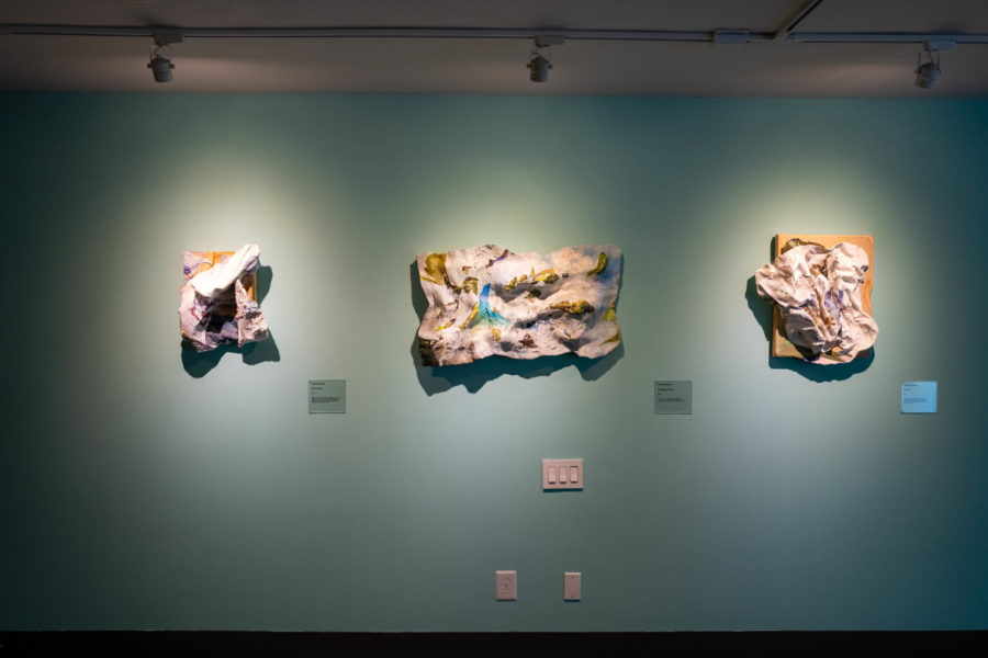 Three molded artworks by Camille Hoffman hang on an aquamarine wall