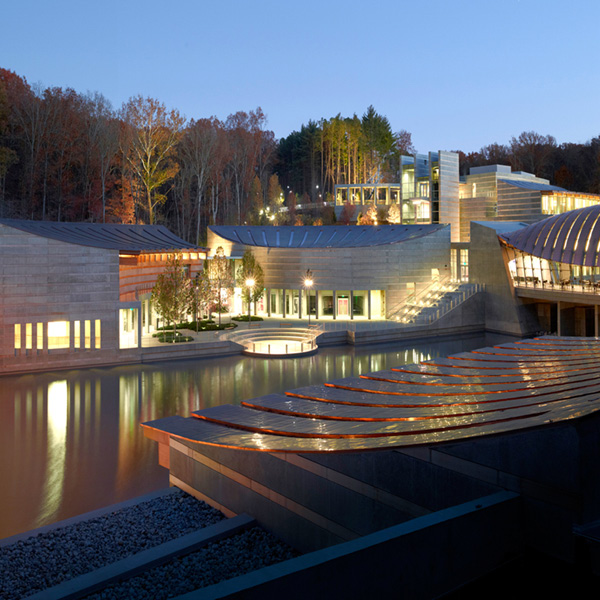 A picture of the Crystal Bridges Museum of American Art, taken at sunset. Undulating metal buildings with a central pond reflecting the light
