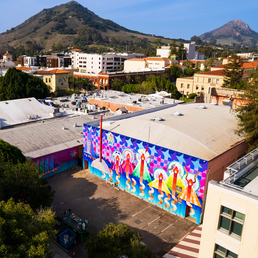 Maria Molteni's mural in downtown SLO. Quilt-like patterns of semi-circles falling down before a minimalistic water background. Geometric mountains with braids of lava, symbolizing the seven sisters of SLO. Seven stars in quilt-like patterns representing the Pleiades are above the mountain peaks.
