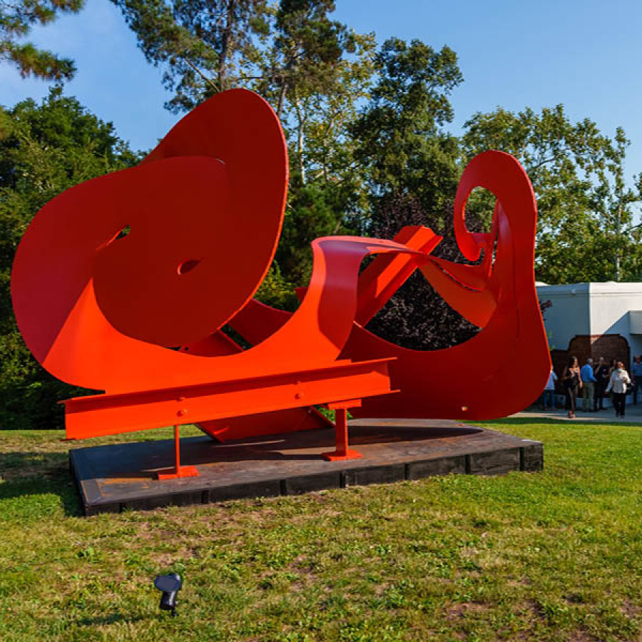 Mama Mobius by artist Mark di Suvero. An abstract steel sculpture evoking the mobius strip, in bright red sits on a lawn. The Museum is in the background.