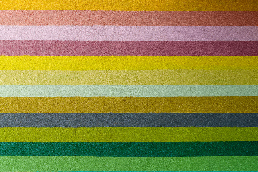Stripes of bright happy colors ranging from orange to pink to yellow to green on a stucco wall