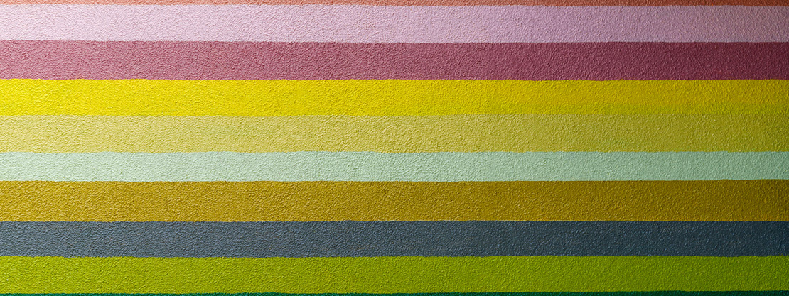 Stripes of bright happy colors ranging from pink to yellow to green on a stucco wall