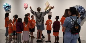 docent group tours web A SLOMA docent gives an exhibition tour to young YMCA campers in orange shirts