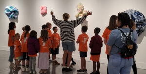 docent group tours web A SLOMA docent gives an exhibition tour to young YMCA campers in orange shirts