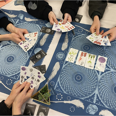 Four young people gather around a table covered in cosmic designs, holding tarot cards