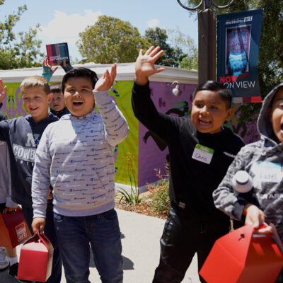 A group of elementary school kids wave at the camera outside the museum