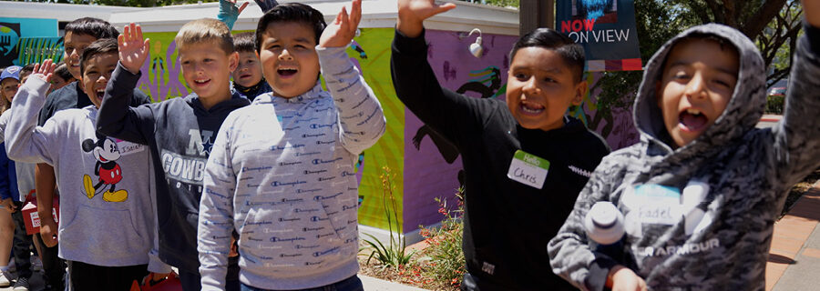 A group of elementary school kids wave at the camera outside the museum