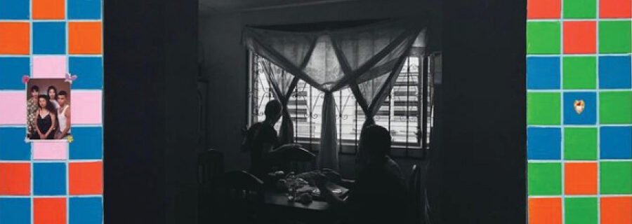A black and white family photo of a couple seated at a table with curtains, surrounded by colorful tiles