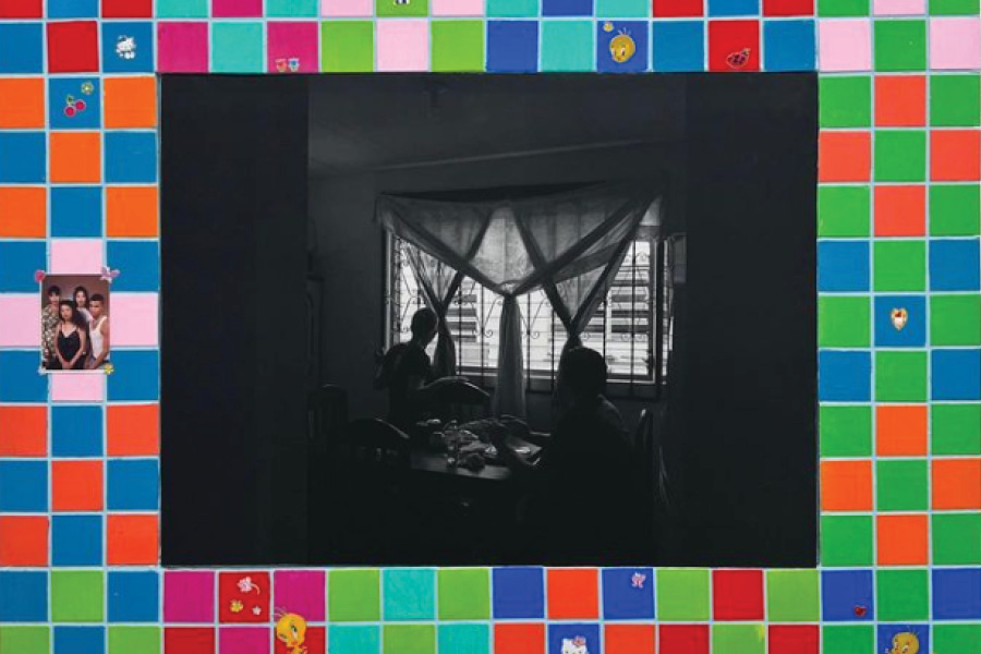 A black and white family photo of a couple seated at a table with curtains, surrounded by colorful tiles