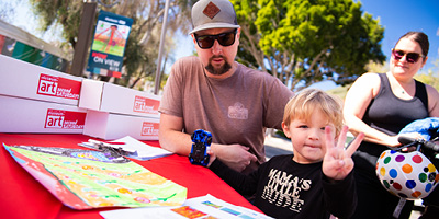 A young family completes an art activity at SLOMA, the young boy has 3 fingers up