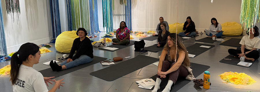 A group of people sit on yoga mats in an exhibition gallery