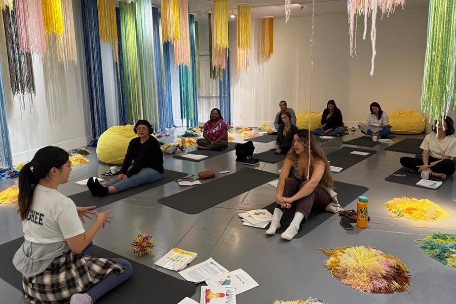 A group of people sit on yoga mats in an exhibition gallery