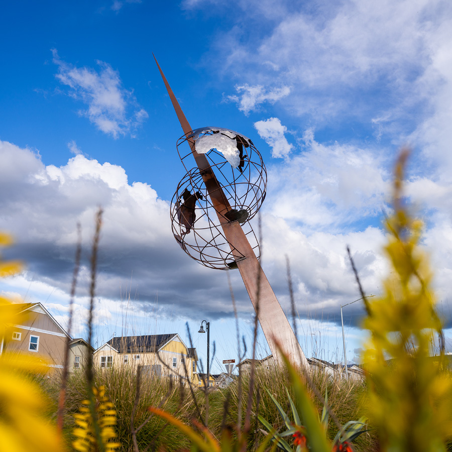 A tall metal sculpture depicting a skyward shard bisecting a globe